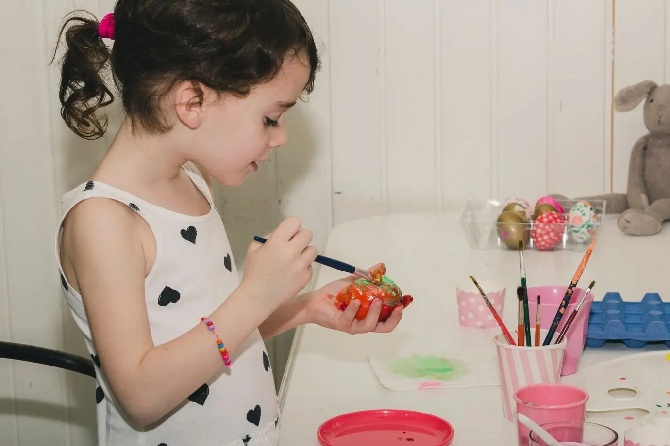 Ein lustiges Mädchen bemalt ein Ei.